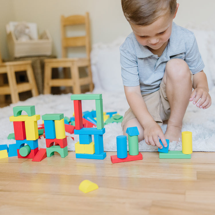 A kid playing with the Melissa & Doug Wooden Building Blocks Set - 100 Blocks in 4 Colors and 9 Shapes