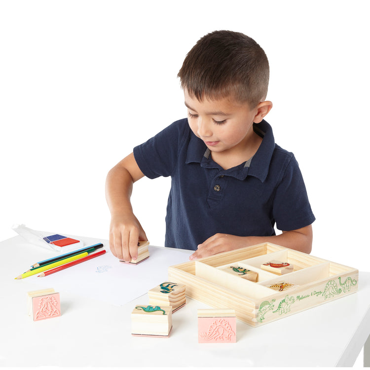 A child on white background with The Melissa & Doug Wooden Stamp Set: Dinosaurs - 8 Stamps, 5 Colored Pencils, 2-Color Stamp Pad