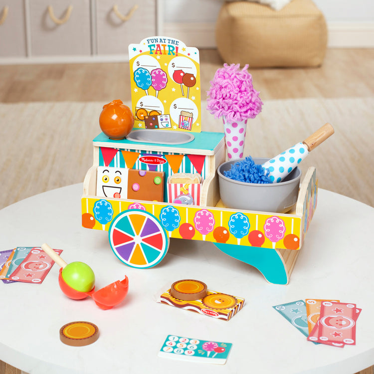 A playroom scene with The Melissa & Doug Fun at the Fair! Wooden Carnival Candy Tabletop Cart and Play Food Set