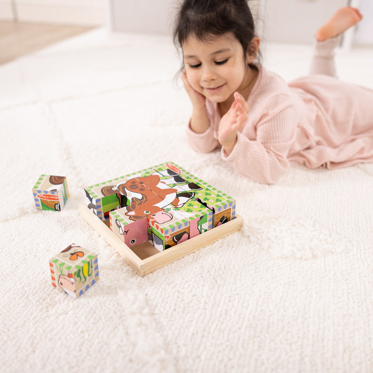 A kid playing with The Melissa & Doug Farm Wooden Cube Puzzle With Storage Tray - 6 Puzzles in 1 (16 pcs)