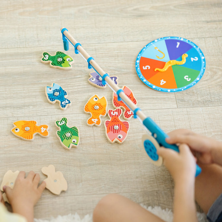 A kid playing with The Melissa & Doug Catch & Count Wooden Fishing Game With 2 Magnetic Rods