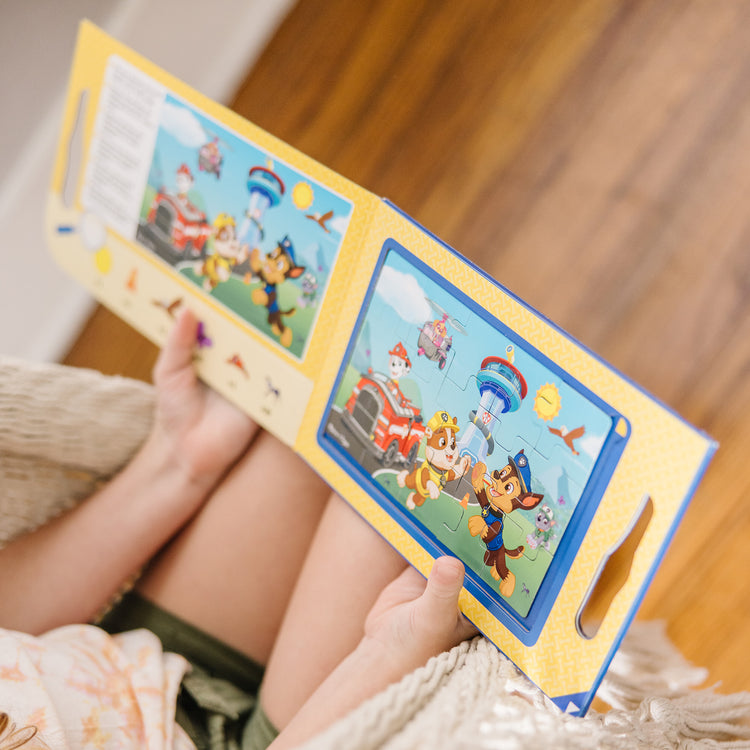 A kid playing with The Melissa & Doug PAW Patrol Take-Along Magnetic Jigsaw Puzzles (2 15-Piece Puzzles)