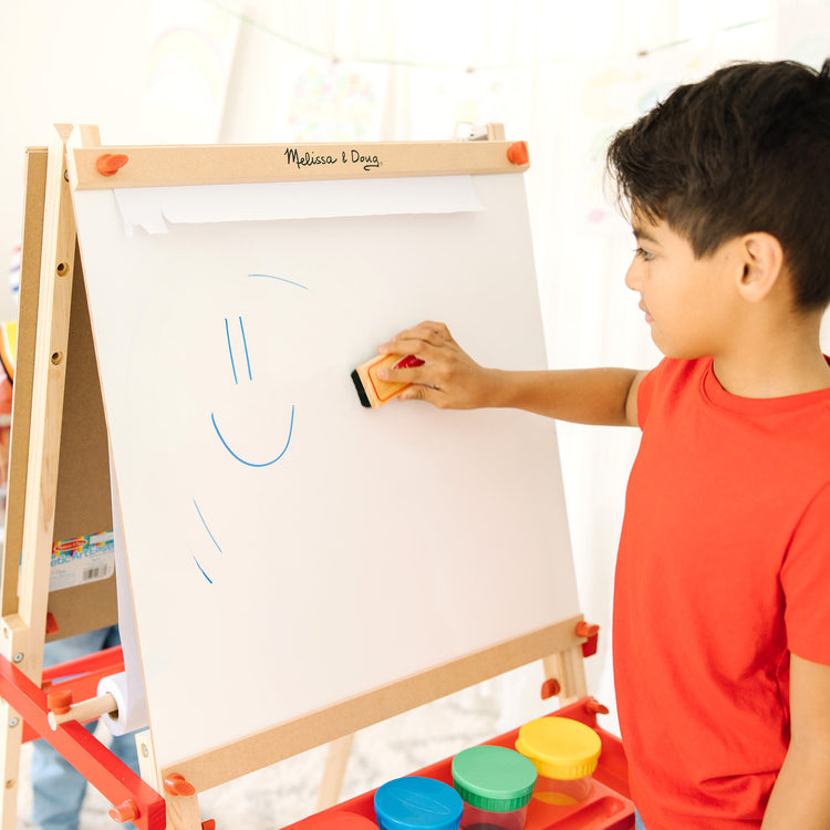 A kid playing with The Melissa & Doug Deluxe Magnetic Standing Art Easel With Chalkboard, Dry-Erase Board, and 39 Letter and Number Magnets