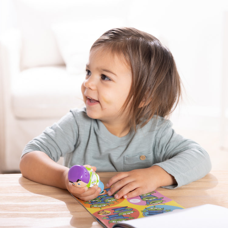 A kid playing with The Melissa & Doug Sticker Wow!™ 24-Page Activity Pad and Sticker Stamper, 300 Stickers, Arts and Crafts Fidget Toy Collectible Character – Disney Buzz Lightyear - for Kids Ages 3+