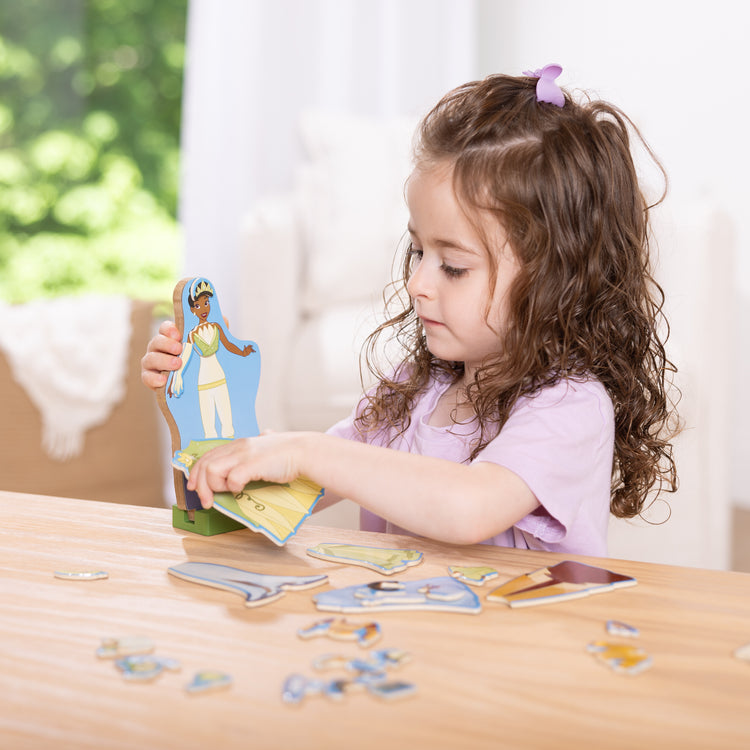 A kid playing with The Melissa & Doug Disney Princess Tiana Magnetic Dress-Up Wooden Doll Pretend Play Set (30+ pcs)
