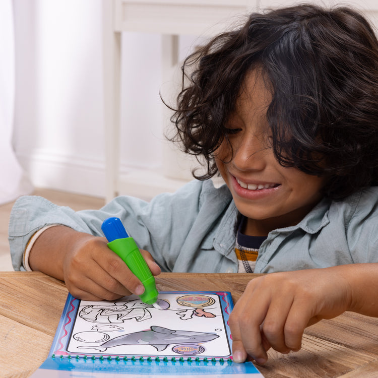 A kid playing with The Melissa & Doug Water WOW! 2-Pack – Animals, Vehicles Water-Reveal Travel Activity Pads 