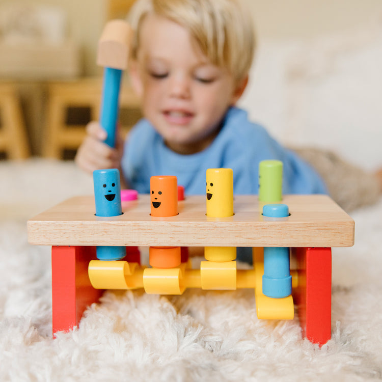 A kid playing with The Melissa & Doug Deluxe Pounding Bench Wooden Toy With Mallet