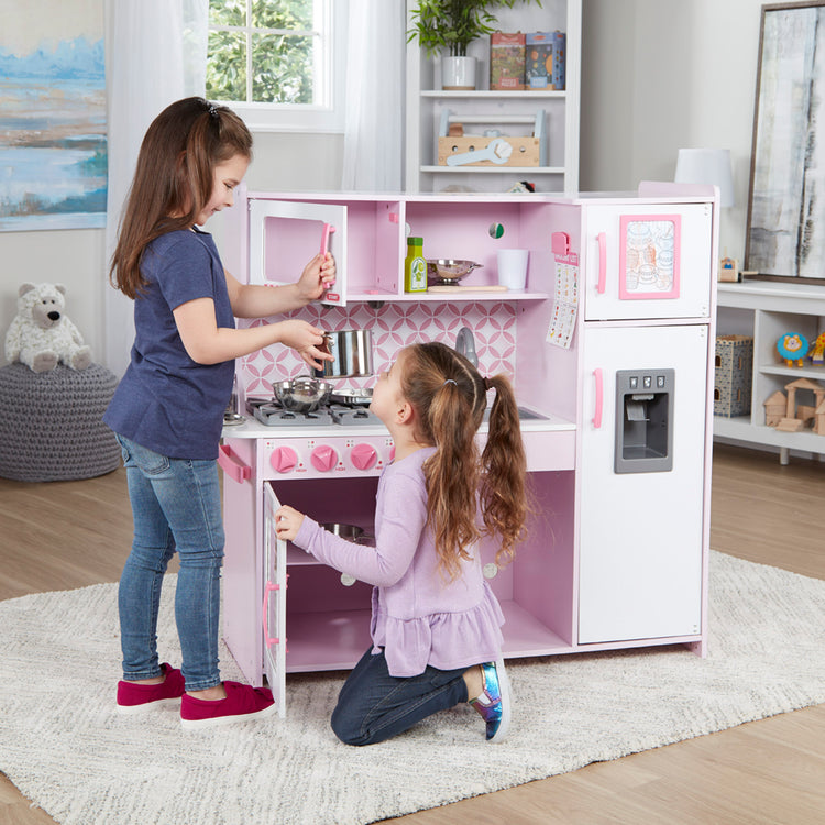 A kid playing with The Melissa & Doug Wooden Chef’s Pretend Play Toy Kitchen With “Ice” Cube Dispenser – Cupcake Pink/White