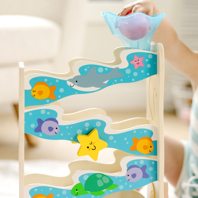 A kid playing with The Melissa & Doug Rollables Wooden Ocean Slide Infant and Toddler Toy (5 Pieces)