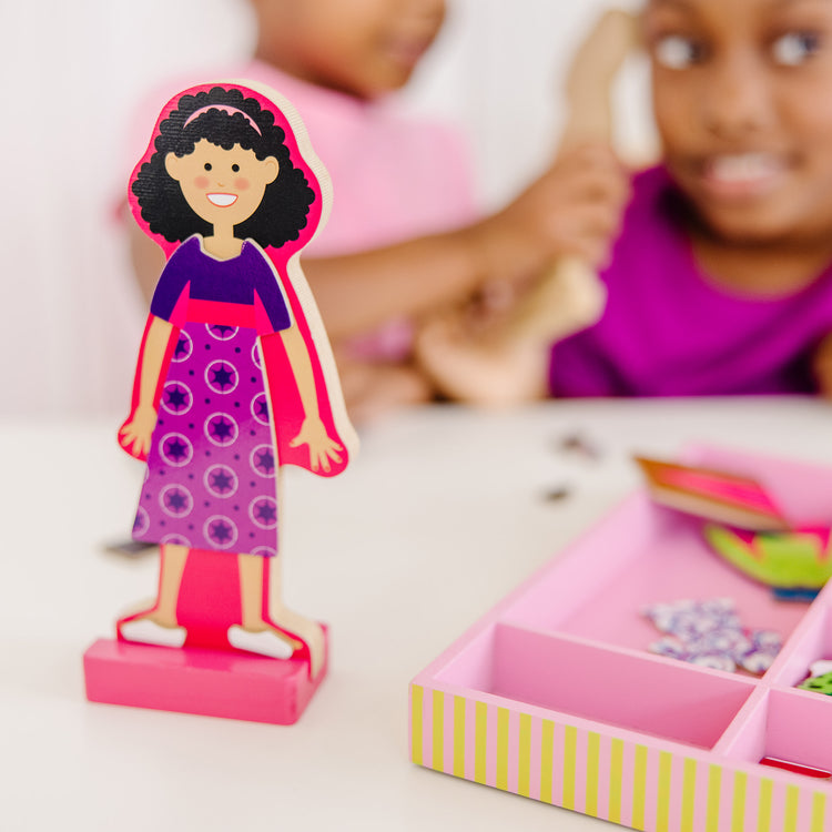 A kid playing with The Melissa & Doug Abby and Emma Deluxe Magnetic Wooden Dress-Up Dolls Play Set (55+ pcs)