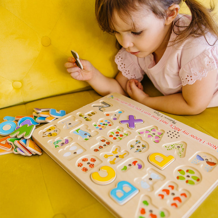A kid playing with The Melissa & Doug Wooden Alphabet Sound Puzzle - Wooden Puzzle With Sound Effects (26 pcs)