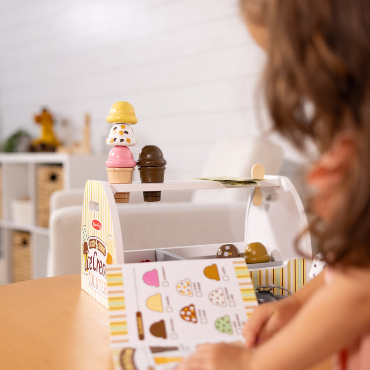 A kid playing with The Melissa & Doug Wooden Scoop and Serve Ice Cream Counter (28 pcs) - Play Food and Accessories