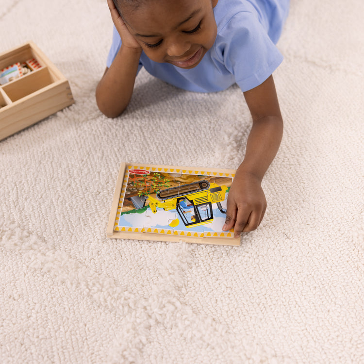 A kid playing with The Melissa & Doug Construction Vehicles 4-in-1 Wooden Jigsaw Puzzles in a Box (48 pcs)