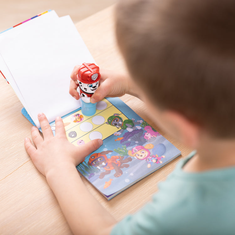 A kid playing with The Melissa & Doug Sticker WOW!™ PAW Patrol Marshall Bundle: 24-Page Activity Pad, Sticker Stamper, 500 Stickers, Mini Pad, Arts and Crafts Fidget Toy Collectible Character