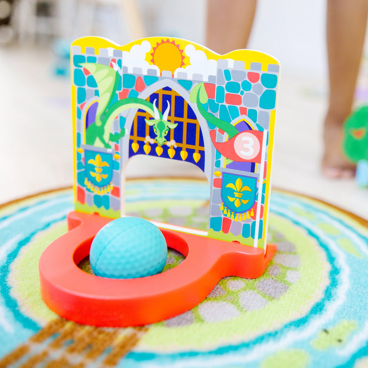 A kid playing with The Melissa & Doug Fun at the Fair! Mini Golf Play Set – 3 Multi-Themed Holes and Wooden Obstacles
