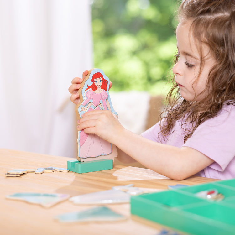 A kid playing with The Melissa & Doug Disney Princess Ariel Magnetic Dress-Up Wooden Doll Pretend Play Set (30+ Pieces)