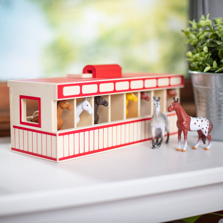 A playroom scene with The Melissa & Doug Take-Along Show-Horse Stable Play Set With Wooden Stable Box and 8 Toy Horses