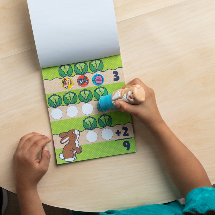 A kid playing with The Melissa & Doug Sticker WOW!™ 24-Page Activity Pad and Sticker Stamper, 300 Stickers, Arts and Crafts Fidget Toy Collectible Character – Bunny