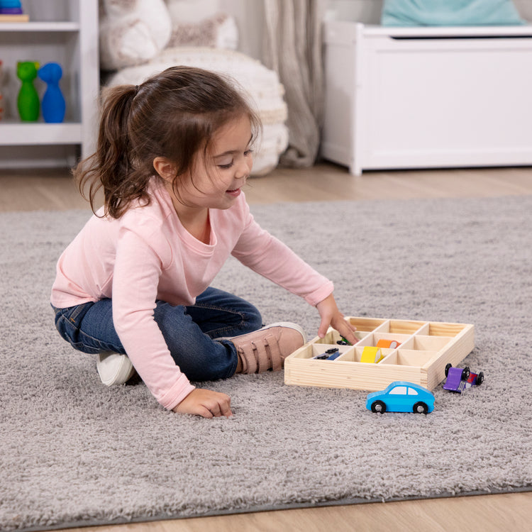 A kid playing with The Melissa & Doug Wooden Cars Vehicle Set in Wooden Tray