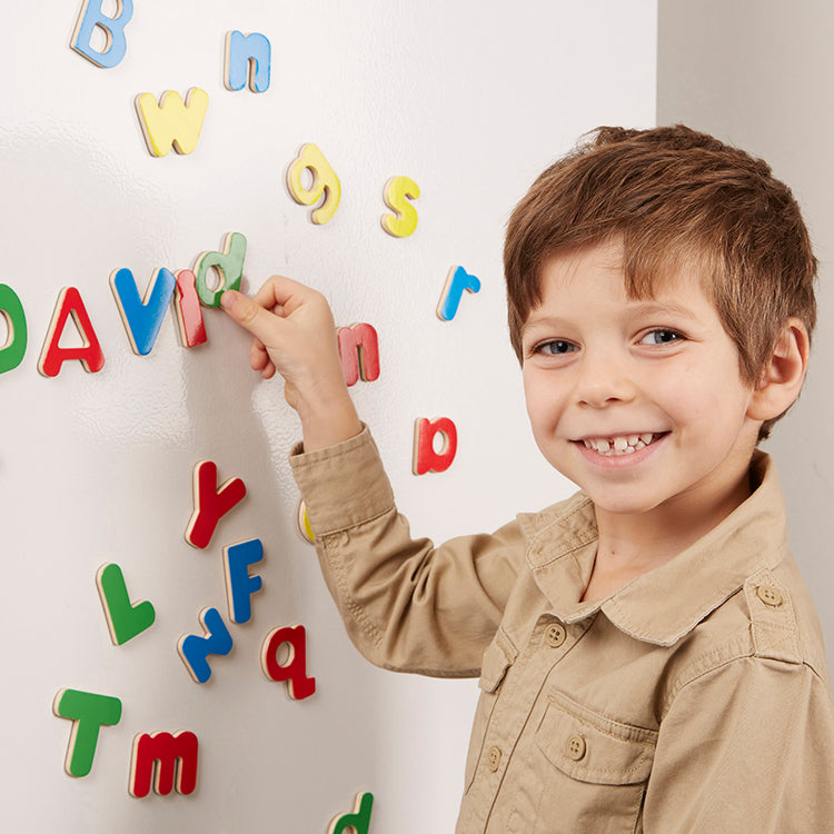 A kid playing with The Melissa & Doug 52 Wooden Alphabet Magnets in a Box - Uppercase and Lowercase Letters