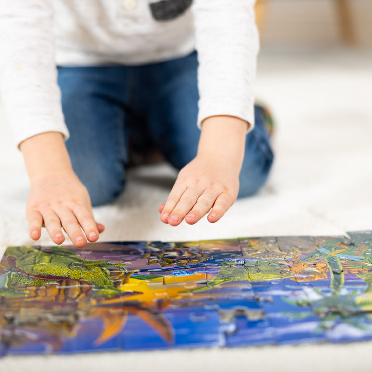 A kid playing with The Melissa & Doug Land of Dinosaurs Jigsaw Puzzle (60 pcs)