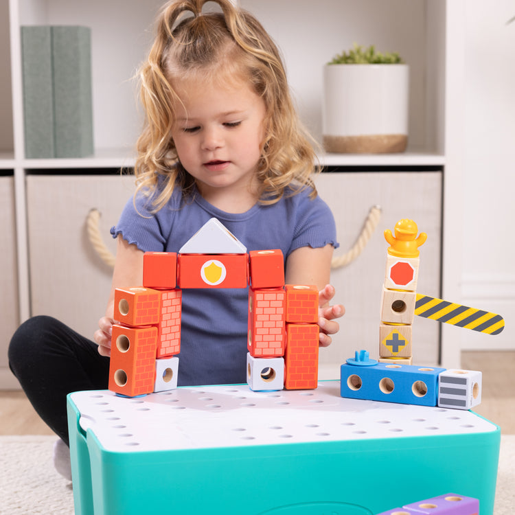 A kid playing with The Melissa & Doug Blockables™ Deluxe City Snap And Play Amazon Exclusive, Mix and Match Connectable Wooden Building Blocks Play Set With Storage Bin and Play Lid (122 Pcs)