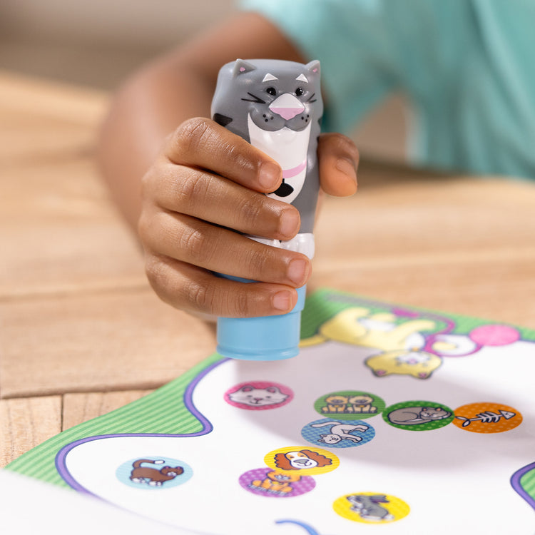 A kid playing with The Melissa & Doug Sticker WOW!™ 24-Page Activity Pad and Sticker Stamper, 300 Stickers, Arts and Crafts Fidget Toy Collectible Character – Cat