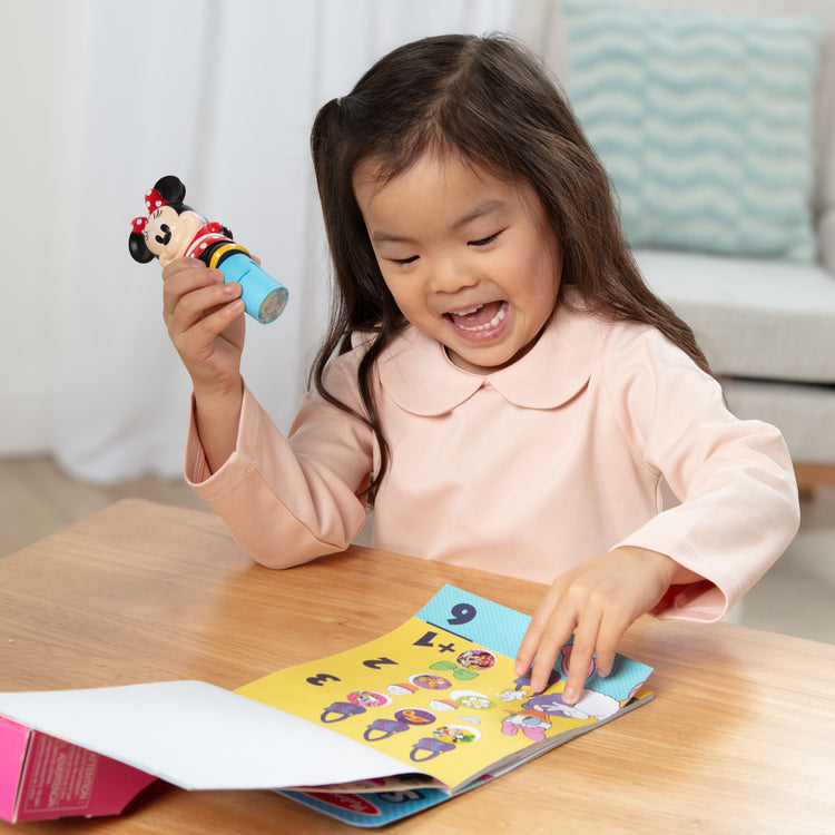 A kid playing with The Melissa & Doug Sticker WOW!™ Disney Minnie Mouse Bundle: 24-Page Activity Pad, Sticker Stamper, 500 Stickers, Mini Pad, Arts and Crafts Fidget Toy Collectible Character