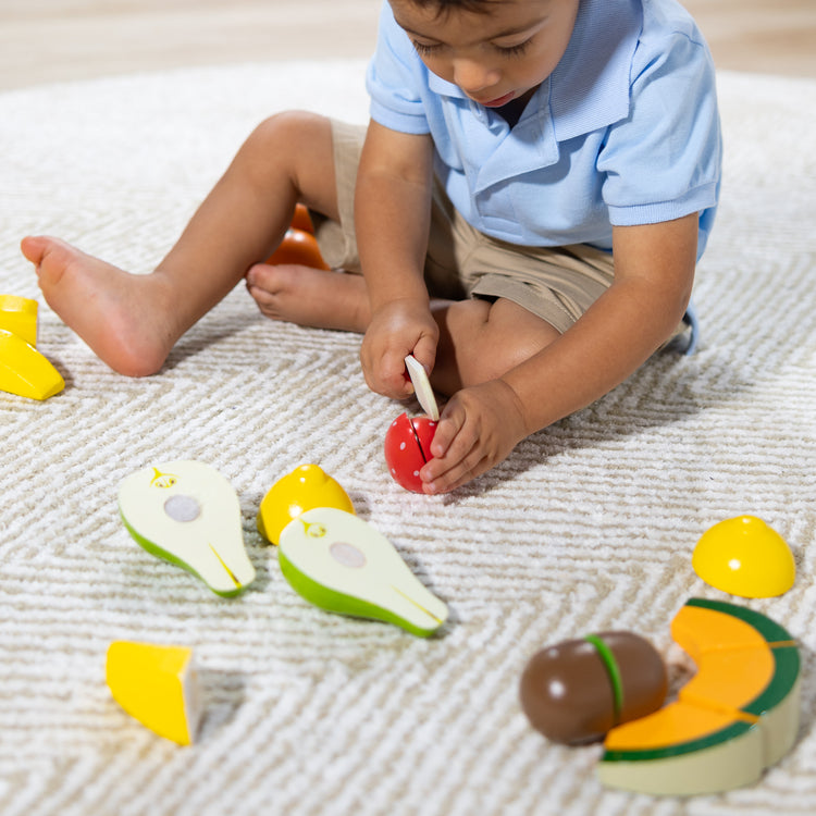 A kid playing with The Melissa & Doug Cutting Fruit Set - Wooden Play Food Kitchen Accessory, Multi