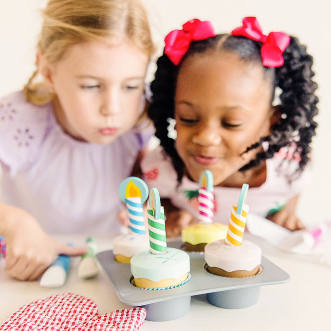 two girls blowing out fake candles on wooden cupcake toys