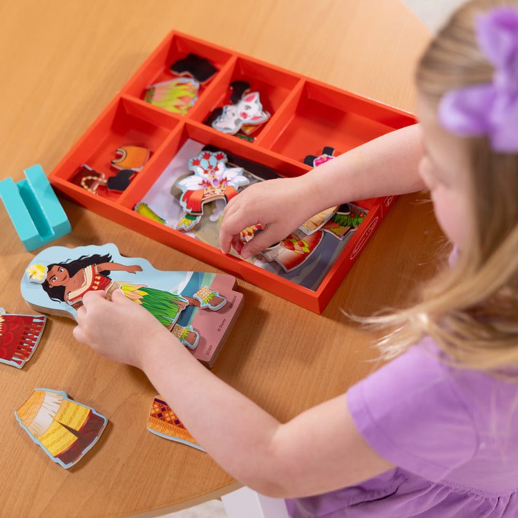 A kid playing with The Melissa & Doug Disney Princess Moana Magnetic Dress-Up Wooden Doll Pretend Play Set (30+ pcs)
