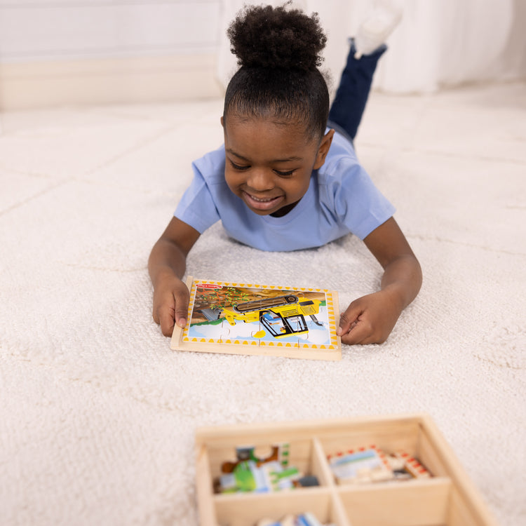 A kid playing with The Melissa & Doug Construction Vehicles 4-in-1 Wooden Jigsaw Puzzles in a Box (48 pcs)