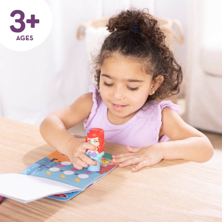 A kid playing with The Melissa & Doug Sticker Wow!™ 24-Page Activity Pad and Sticker Stamper, 300 Stickers, Arts and Crafts Fidget Toy Collectible Character – Disney Princess Ariel - for Kids Ages 3+