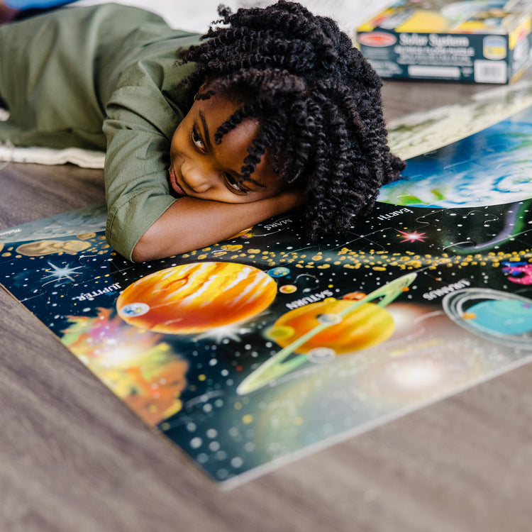 A kid playing with The Melissa & Doug Solar System Floor Puzzle (48 pcs, 2 x 3 Feet)