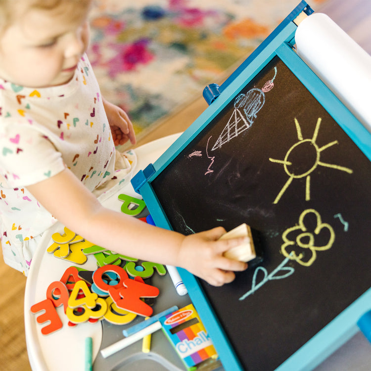 A kid playing with The Melissa & Doug Double-Sided Magnetic Tabletop Art Easel - Dry-Erase Board and Chalkboard