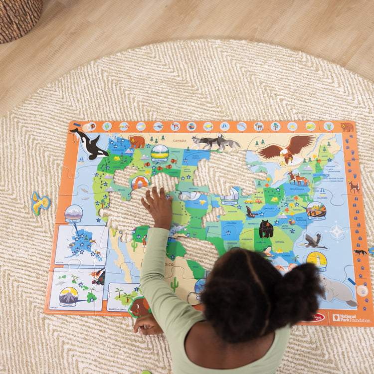 A kid playing with The Melissa & Doug National Parks U.S.A. Map Floor Puzzle – 45 Jumbo and Animal Shaped Pieces, Search-and-Find Activities, Park and Animal ID Guide