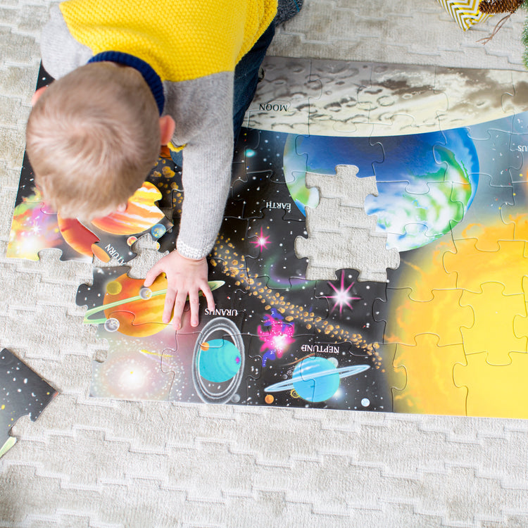 A kid playing with The Melissa & Doug Solar System Floor Puzzle (48 pcs, 2 x 3 Feet)