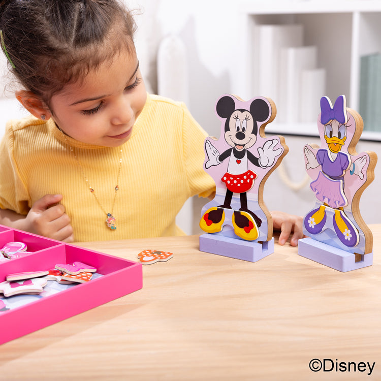 A kid playing with The Melissa & Doug Disney Minnie Mouse and Daisy Duck Deluxe Wooden Magnetic Dress-Up; 2 Fashion Dolls with Stands for Pretend Play, 52 Pieces
