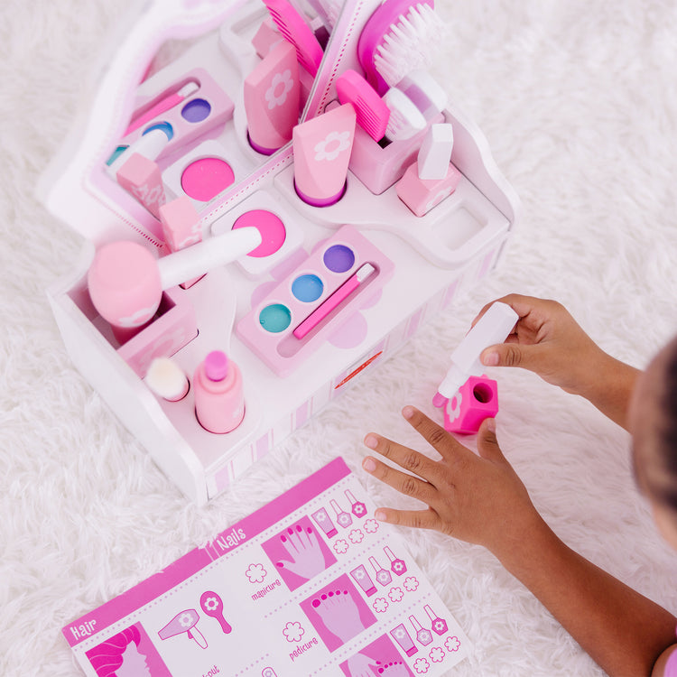 A kid playing with The Melissa & Doug Wooden Beauty Salon Play Set With Vanity and Accessories (18 pcs)