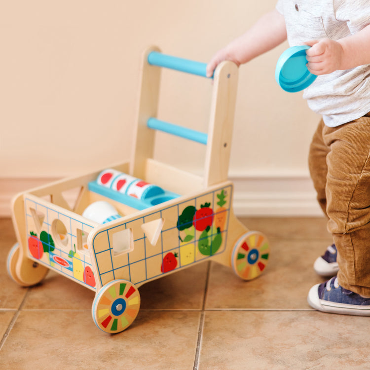 A kid playing with The Melissa & Doug Wooden Shape Sorting Grocery Cart Push Toy and Puzzles