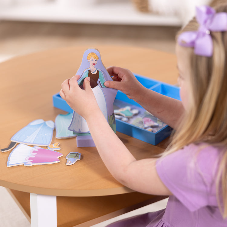 A kid playing with The Melissa & Doug Disney Princess Cinderella Magnetic Dress-Up Wooden Doll Pretend Play Set (30+ pcs)