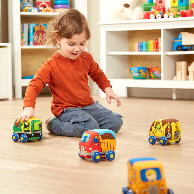 A kid playing with The Melissa & Doug Pull-Back Construction Vehicles - Soft Baby Toy Play Set of 4 Vehicles