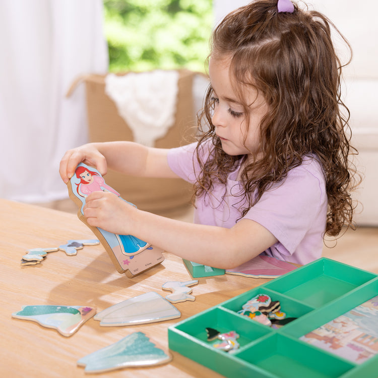 A kid playing with The Melissa & Doug Disney Princess Ariel Magnetic Dress-Up Wooden Doll Pretend Play Set (30+ Pieces)