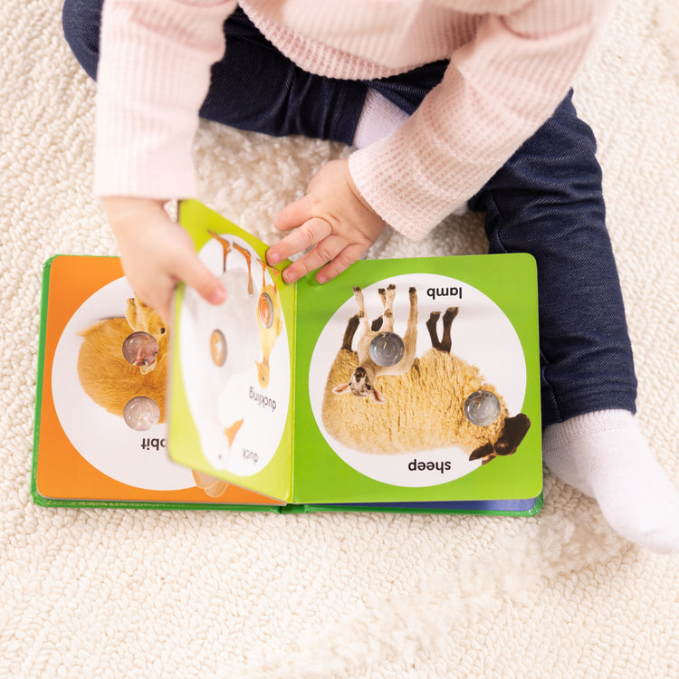 A kid playing with The Melissa & Doug Children’s Book – Poke-a-Dot: Farm Animal Families (Board Book with Buttons to Pop)