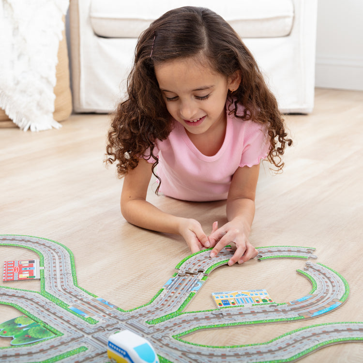 A kid playing with The Melissa & Doug Design Your Own Railroad 48-Piece Floor Puzzle with 2 Wind-up Toy Trains and Interchangeable Scenery, Kids Puzzles with Preschool Toys for Girls & Boys Ages 4 and Up