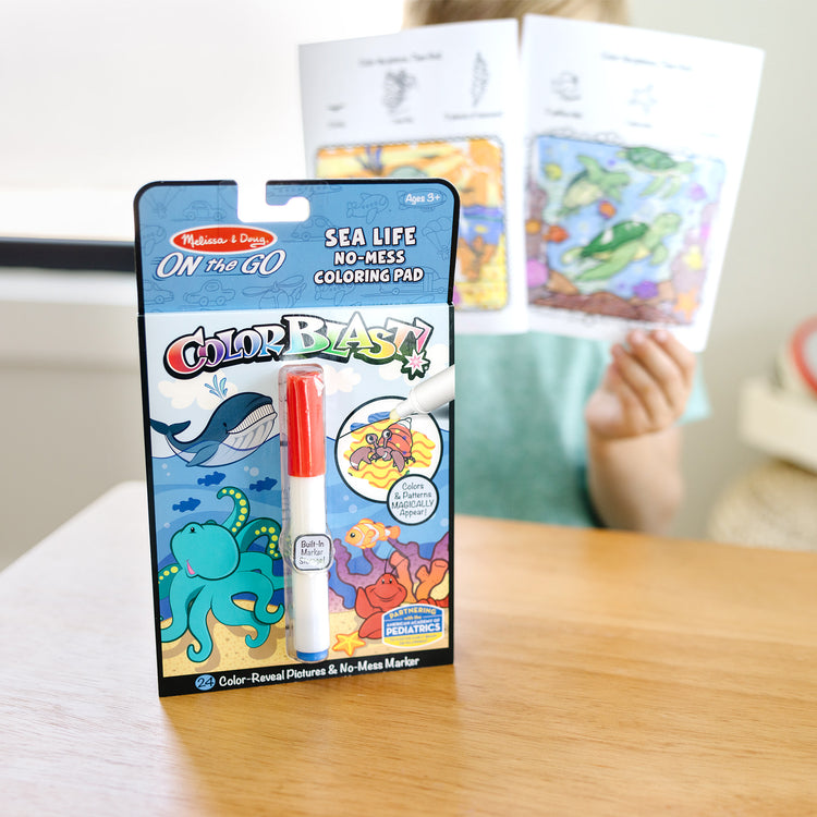 A kid playing with The Melissa & Doug On the Go ColorBlast! Activity Book: Sea Life - 24 Pictures and No-Mess Pen