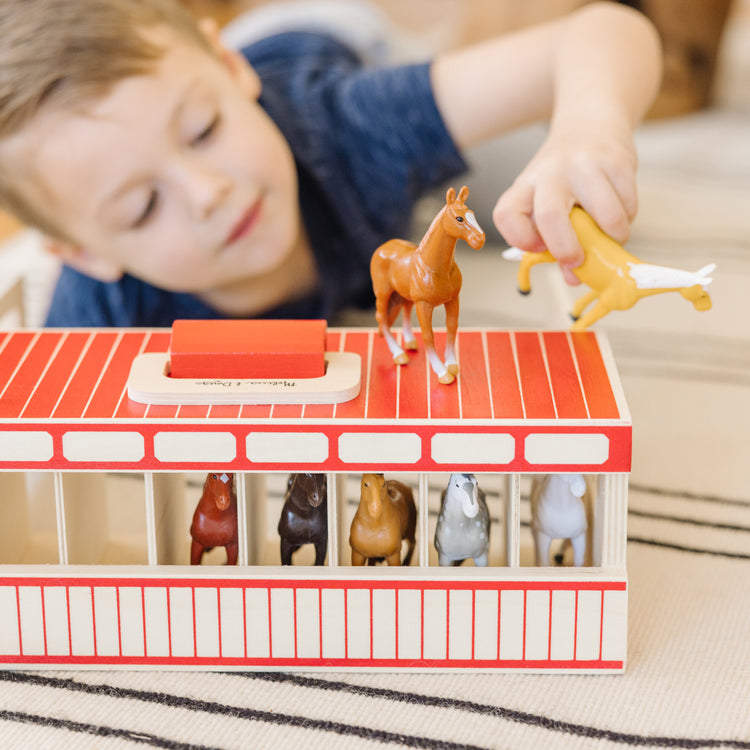 A kid playing with The Melissa & Doug Take-Along Show-Horse Stable Play Set With Wooden Stable Box and 8 Toy Horses
