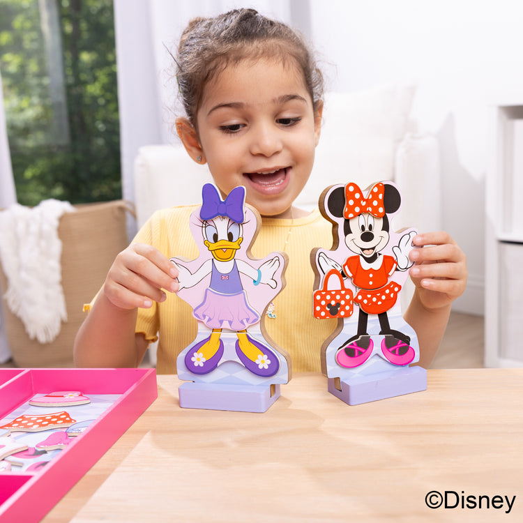 A kid playing with The Melissa & Doug Disney Minnie Mouse and Daisy Duck Deluxe Wooden Magnetic Dress-Up; 2 Fashion Dolls with Stands for Pretend Play, 52 Pieces