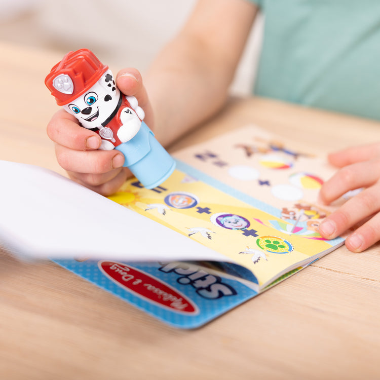 A kid playing with The Melissa & Doug Sticker WOW!™ 24-Page Activity Pad and Sticker Stamper, 300 Stickers, Arts and Crafts Fidget Toy Collectible Character – PAW Patrol Marshall