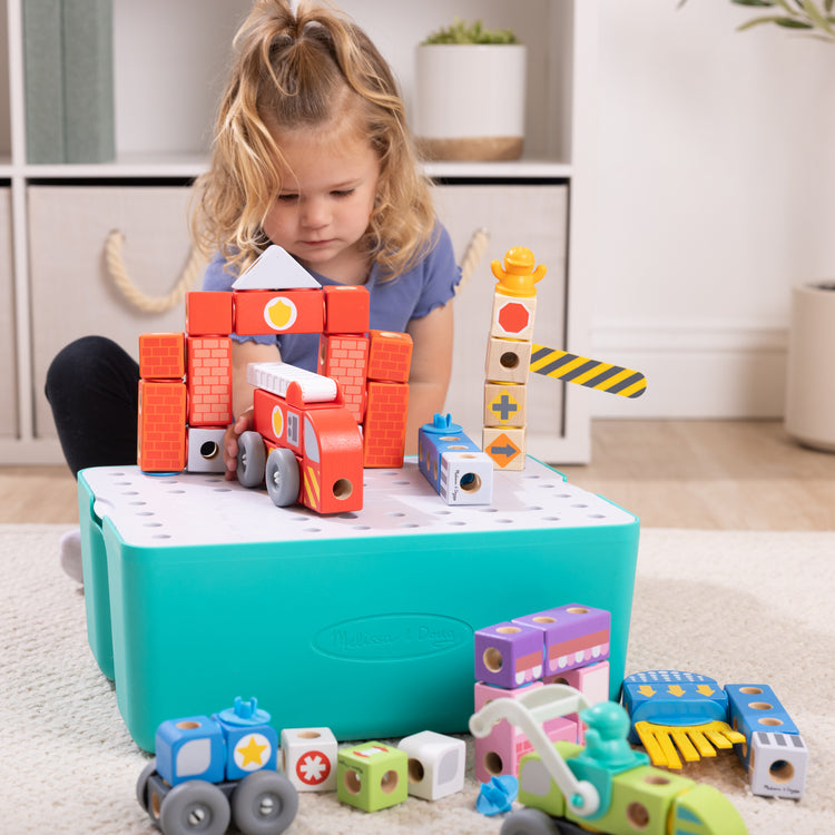 A kid playing with The Melissa & Doug Blockables™ Deluxe City Snap And Play Amazon Exclusive, Mix and Match Connectable Wooden Building Blocks Play Set With Storage Bin and Play Lid (122 Pcs)